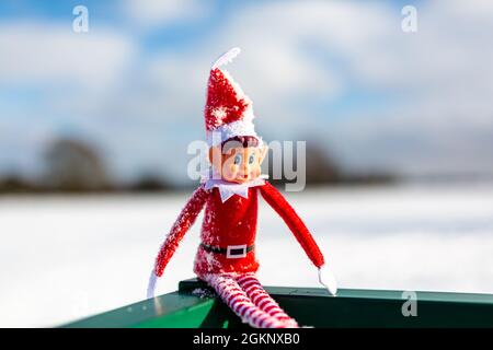 A close up of a naughty Christmas elf sitting outside in the snowy winter landscape enjoying the winter sunshine. Elf on the shelf, naughty, christmas Stock Photo