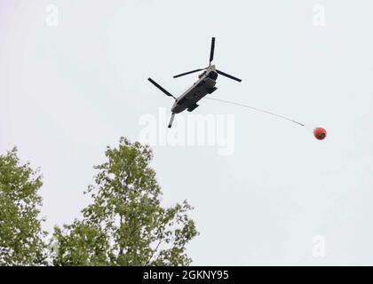 A 1st Battalion, 207th Aviation Regiment CH-47 Chinook helicopter with a Bambi water bucket system attached flies overhead during the unit's Red Card certification on Joint Base Elmendorf-Richardson, June 9, 2021. Red Card certification, also known as the Incident Qualification Card, is an accepted interagency certification that a person is qualified in order to accomplish the required mission when arriving on an incident. For 1-207th AVN pilots, this certification means proficiency in water bucket drops to assist with wildfire emergencies within the state. Stock Photo