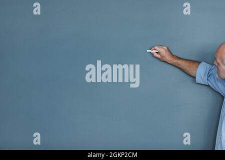 Senior teacher or businessman writing on a blank chalkboard while teaching a class, doing training or giving a presentation with large copyspace on th Stock Photo