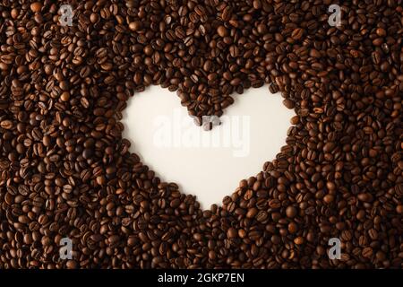 Pile of coffee beans with hollow on a white table forming the shape of a heart. Top view. Horizontal composition. Stock Photo