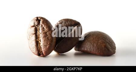 Macro view of three coffee beans reflected on white table and white background. Front view. Horizontal composition. Stock Photo