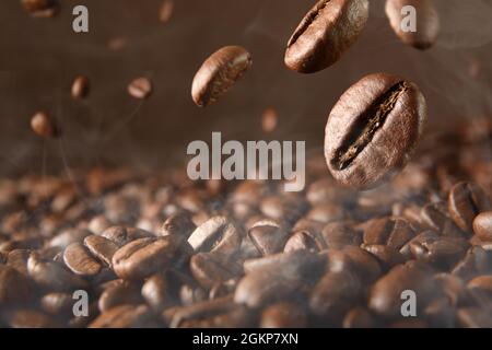 Roasted hot coffee beans falling on pile of coffee beans. Front view. Horizontal composition. Stock Photo