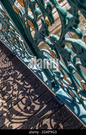 Wrought iron decorative fence on bridge. Forming an interesting design with it's cast shadow on the floor. Selective focus. Stock Photo