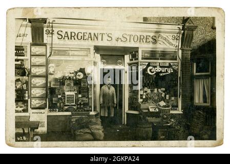 Original 1920's postcard of a proprietor shopkeepter outside his shopfront, Sargeant's Stores & Provisions,ads for Rinso, Cadbury's cocoa, Bovril, Champions vinegar, 92 Brockley Road, South London, U.K. in 1924 Stock Photo