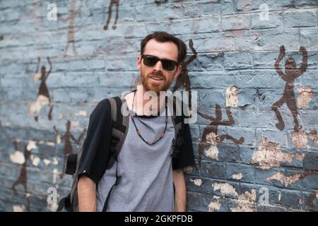 Young man with beard and sunglasses standing near the wall outdoors. Stock Photo