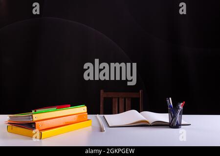 Pencils pot next to the stacked books and an open notebook , school supplies on white desk with blackboard texture in background. Side view, copy spac Stock Photo