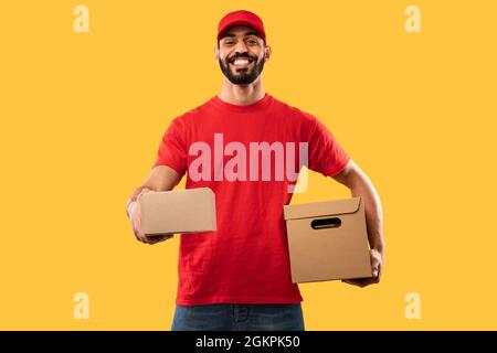 Arab Courier Guy Delivering Cardboard Boxes Over Yellow Studio Background Stock Photo