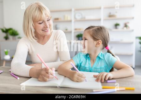 Portrait granny and granddaughter spending time at home, drawing Stock Photo