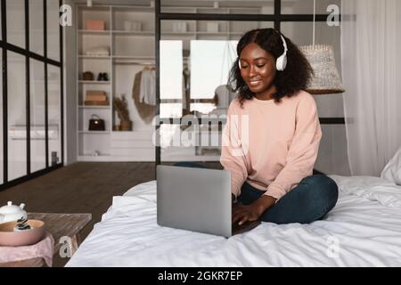 African Female Using Laptop Wearing Headphones Working Online At Home Stock Photo