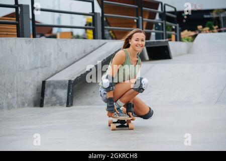 Playful pretty blonde on skate rolling in a low stance at skatepark Stock Photo