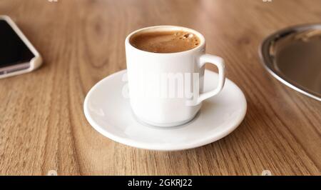 Traditional Turkish coffee in small white cup on wooden table - Image Stock Photo