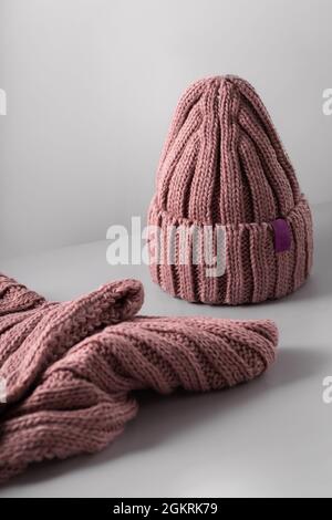 Small red knitted hat with on a white scarf jn grey background. woolly hat Closeup. Copy space Stock Photo