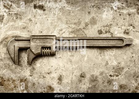 Sepia toned image of a vintage rusty adjustable spanner on an old iron background Stock Photo
