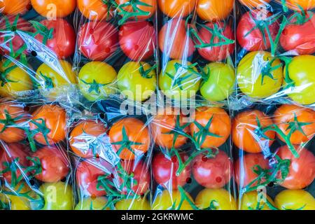 Display of fresh plastic wrapped yellow, orange and red cherry tomatoes Stock Photo