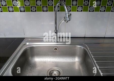The clean metal sink with the chrome tap after washing on the modern counter, inside the kitchen of the urban house,  front view for the copy space. Stock Photo