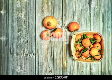 Top view image of wooden basket with ripe fruit, mandarinas with green leaves, persimmons and pomegranate on wooden planks Stock Photo