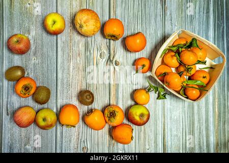 Top view image of apples, kiwis, ripe persimmons, pomegranates and basket of tangerines on wooden table Stock Photo