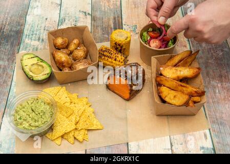 Chef's hands placing onion on a salad in a set of Mexican-style takeout plates with avocado, tortilla chips, guacamole, roasted sweet potato, grilled Stock Photo