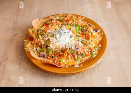 Plate of nachos with guacamole, beans and baked melted cheese on wooden table Stock Photo