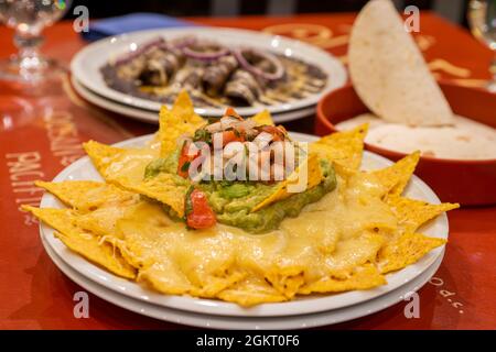 Corn nachos with melted cheese, avocado guacamole, onion and chopped tomato served on a table in a Mexican restaurant Stock Photo