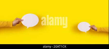 two talk bubbles speech icon in hand over yellow background, panoramic layout Stock Photo