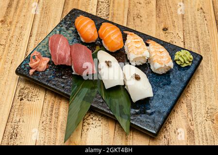 Beautiful black tray with blue sparkles with banana leaves and typical Japanese recipe for butterfish nigiri with truffle, prawn nigiri, Norwegian sal Stock Photo