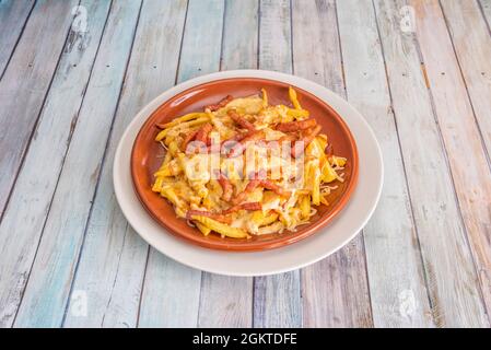 Clay plate with french fries and bacon strips with melted grated cheese on wooden table Stock Photo