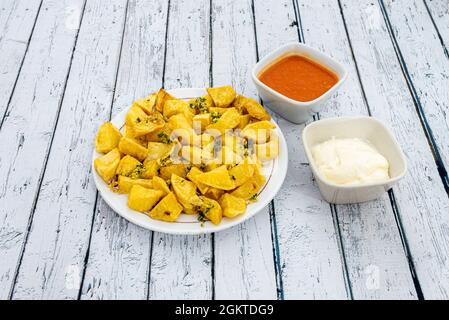 Portion of potato chips seasoned with salt, garlic and parsley and with two dipping sauces on a white wooden table Stock Photo