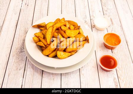 Ration of potato chips wedges with assorted sauces for dipping on white wooden table Stock Photo