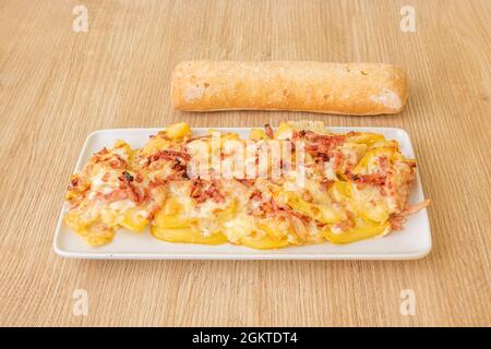 French fries with bacon strips and melted cheese with a rustic loaf of bread on a white plate Stock Photo