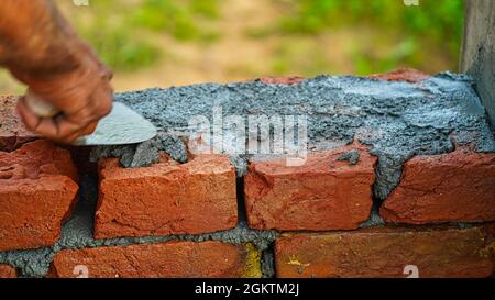 Bricklayer worker installing brick masonry on exterior wall with trowel putty knife local county in India. Stock Photo