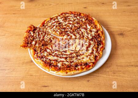 Pizza with barbecue sauce in circles with a lot of minced meat, a lot of melted cheese and a slice cut on a white plate Stock Photo