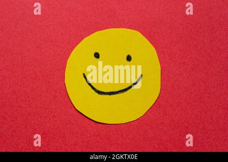 Hand drawn smiling face on yellow sticker. Happy face on paper isolated on red background. Stock Photo
