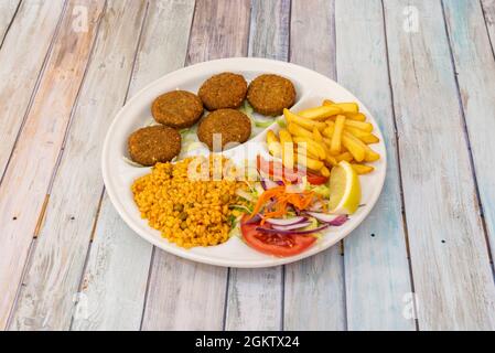 Falafel plate menu in kebab restaurant with bulgur stew, fried potatoes, salad with red onion, grated carrot, tomato slices and lemon wedges on white Stock Photo