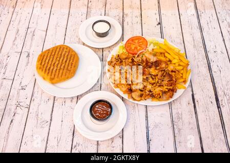 Kebab menu on plate with roast chicken meat with fried potatoes, salad with tomato and fresh lettuce with onion. Grilled pita bread, tomato sauce and Stock Photo