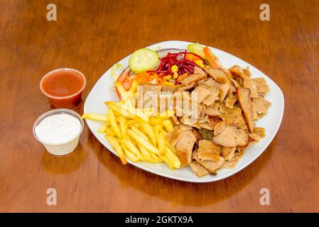 Kebab menu on plate with fried potatoes, chopped roast lamb doner, beetroot, carrot, cucumber and red onion salad with red and white sauce Stock Photo