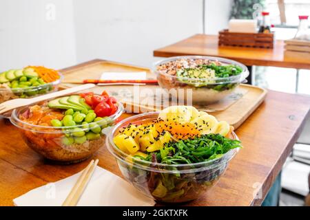 Various home delivery containers with various poke bowl ingredient configurations. Diced mango, marinated salmon, wakame seaweed salad, tamates, flamb Stock Photo