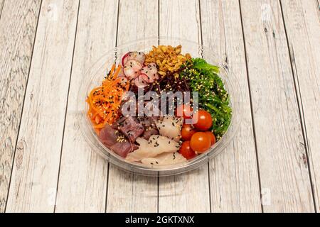 Transparent poke bowl with cherry tomatoes, wakame salad, red tuna tacos, butterfish chunks, crispy onion, grated carrot, shredded beets, sliced radis Stock Photo