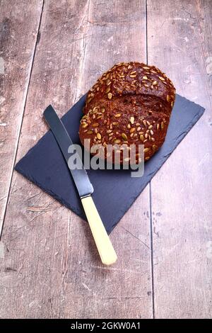Freshly baked Pumpernickel Boule artisan bread  laid on a wooden table with a old bred knife Stock Photo