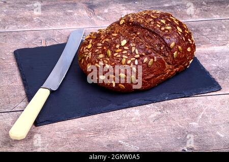 Freshly baked Pumpernickel Boule artisan bread with buttered bread slices cut and laid on a wooden table with a old bred knife Stock Photo