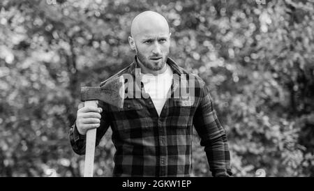 Determination of human spirit. Man checkered shirt use axe. Brutal male in forest. Power and strength. Lumberjack carry ax. Bald woodsman. Harvest Stock Photo