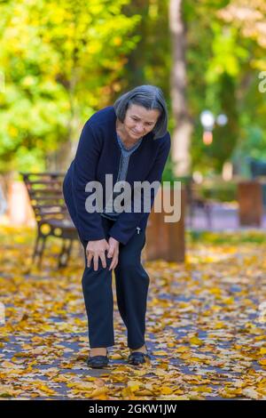 Senior woman having knee pain walking in park Stock Photo