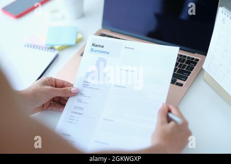 Woman sitting at table in front of laptop and holding paper with resume for employment in her hands Stock Photo