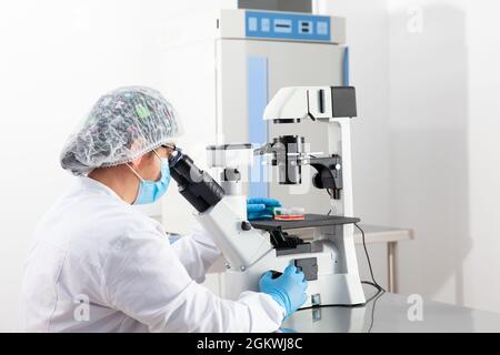 Young female scientist looking at samples under the microscope Stock Photo