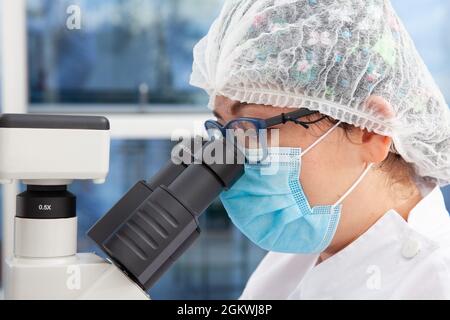 Young female scientist looking at samples under the microscope Stock Photo