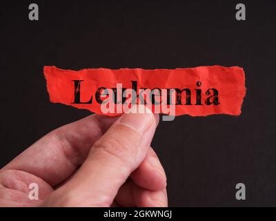 A man holding a piece of red paper with the word Leukemia on it. Close up. Stock Photo