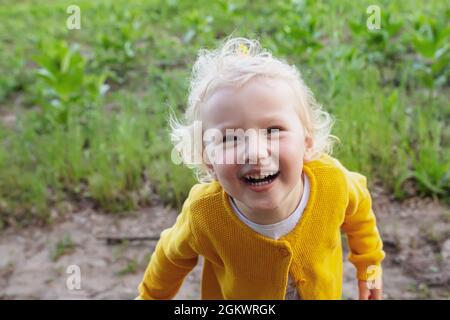 Close-up portrait happy girl in yellow jacket looks up. cheery smart clever child smiles raising face to mother