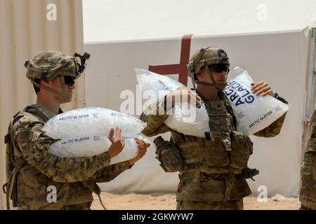 Soldiers assigned to the 45th Infantry Brigade Combat Team, Oklahoma Army National, carry ice to hydration stations during annual training at the National Training Center at Fort Irwin, California, July 14, 2021. Members of the 45th IBCT work against the 100-degree temperatures at NTC by keeping ice sheets, hydration systems and cool-off stations filled and ready. Stock Photo