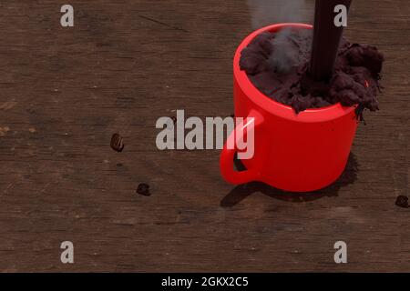 Cup of coffee with chocolate forming the splash while a jet of coffee falls hard into the red cup on a rustic wooden table in Mexico City coffee beans Stock Photo