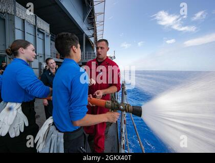 Aviation Maintenance Administrationman 3rd Class Cody Mulligan, from Lake Stevens, Washington, assigned to USS Gerald R. Ford’s (CVN 78) aircraft intermediate maintenance department, instructs Sailors on proper hose handling techniqes on the fantail, July 15, 2021. Ford is underway in the Atlantic Ocean conducting Full Ship Shock Trials. The U.S. Navy conducts shock trials of new ship designs using live explosives to confirm that our warships can continue to meet demanding mission requirements under the harsh conditions they might encounter in battle. Stock Photo